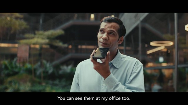 Video Reference: man, smartphone, indoor, office, atrium, portrait, business, modern, speaking, subtitle, technology, casual shirt, interior, corporate, communication