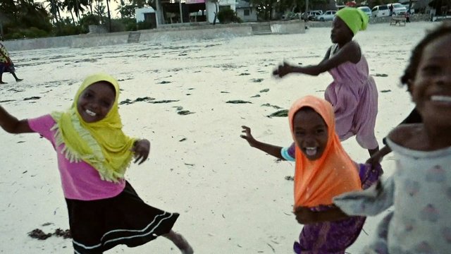 Video Reference: children, beach, playing, dancing, sand, ocean, headscarf, colorful clothing, outdoor, joy, group, motion, shoreline, daytime