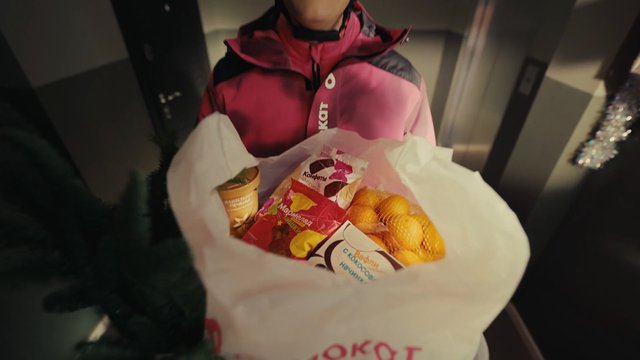 Video Reference: person, shopping bag, groceries, snacks, candies, oranges, winter jacket, indoor, elevator, close-up, package, food, delivery, portrait, retail, carry