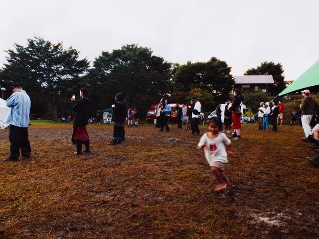 Video Reference: outdoor, gathering, crowd, field, muddy ground, tents, trees, child, running, festival, rural, evening, people, grass, camping, event