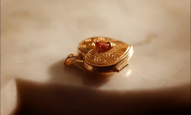 Video Reference: jewelry, gold, pendant, locket, gemstone, red stone, ornate, close-up, macro, luxury, accessory, decorative, metal, shallow depth of field