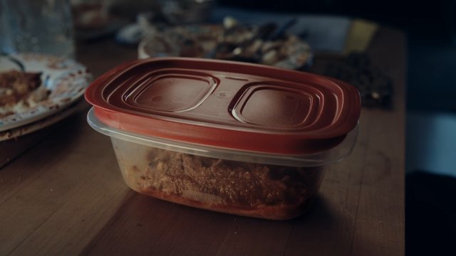 Video Reference: food container, plastic tub, red lid, leftovers, tabletop, kitchen, storage, meal prep, close-up, indoor, homemade food, blurred background