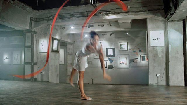 Video Reference: dancer, dance studio, motion blur, white dress, ribbon, performance, indoor, wood floor, art gallery, concrete wall, framed art, movement, acrobatics, studio lighting