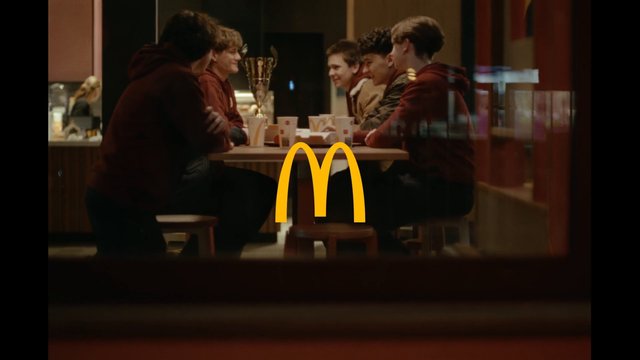 Video Reference: fast food, restaurant, teenagers, group, table, indoor, socializing, cups, trays, meeting, dining, logo, McDonald's, warm lighting, casual