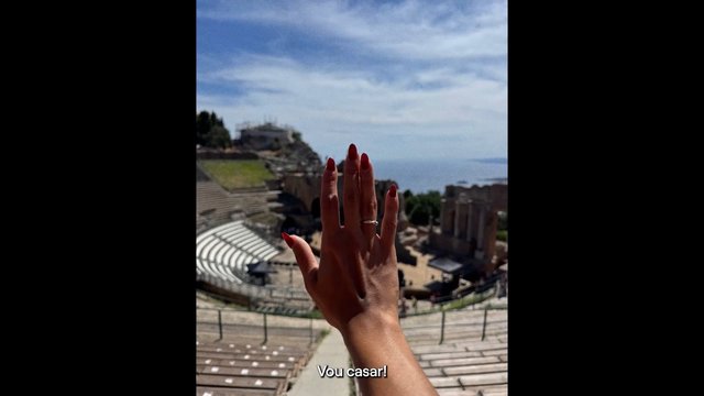 Video Reference: hand, red nails, ring, seaside, amphitheater, ruins, ocean view, outdoor, tourism, travel, landscape, sky, person, gesture, vertical video, subtitle