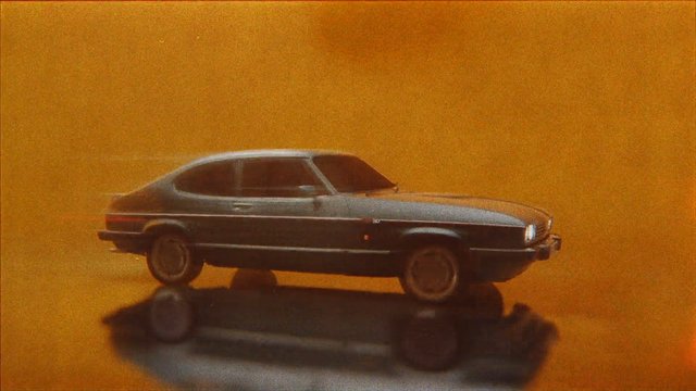 Video Reference: car, model car, sedan, side view, reflection, orange background, toy, vehicle, studio shot, isolated, miniature, dark car
