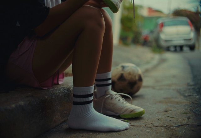Video Reference: soccer, football, street, curb, athlete, shoes, socks, ball, outdoor, urban, resting, sports, blurred background, low angle