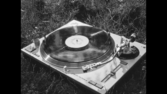 Video Reference: turntable, record player, vinyl record, spinning record, tonearm, music, audio equipment, outdoors, grass, black and white, close-up, retro, analog