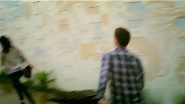 Video Reference: people, walking, outdoor, wall, stone wall, motion blur, back view, casual clothing, street, blurred, daytime, urban