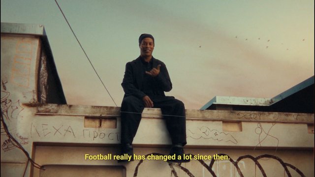 Video Reference: man, rooftop, graffiti, sunset, outdoor, sitting, gesture, smiling, subtitles, urban, sky, ledge, dark clothing, city, evening