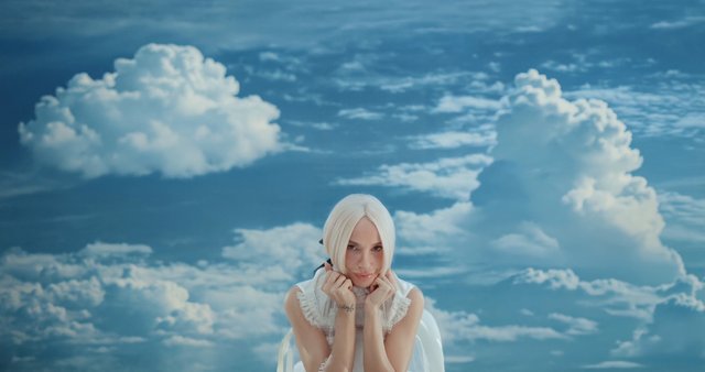 Video Reference: person, blonde hair, portrait, clouds, sky, studio backdrop, centered, fashion, close-up, blue background, pose, soft lighting