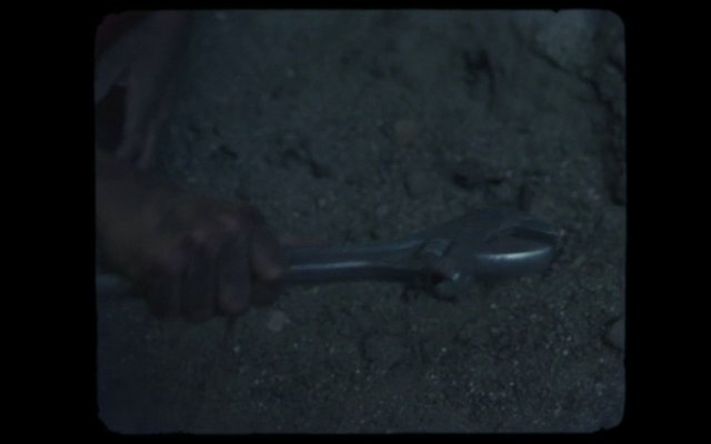 Video Reference: hand, wrench, tool, metal, ground, dark, low light, close-up, work, repair, manual labor, outdoor