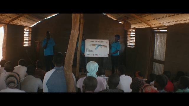 Video Reference: Projection screen, Projector accessory, Stage equipment, Event, T-shirt, Chair, Curtain, Display device, Suit, Crowd