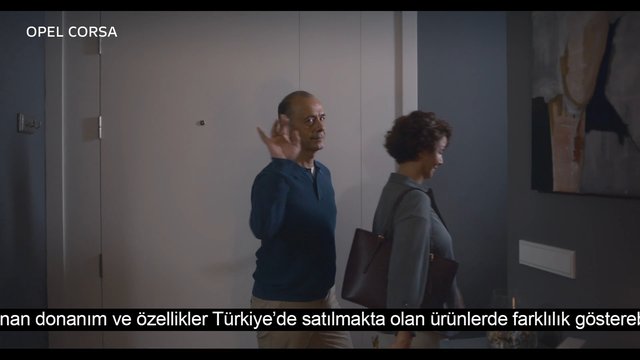 Video Reference: indoor, hallway, two people, man waving, woman walking, door, wall art, subtitles, OPEL CORSA, home interior, entryway, casual clothing, shoulder bag, advertisement, video frame