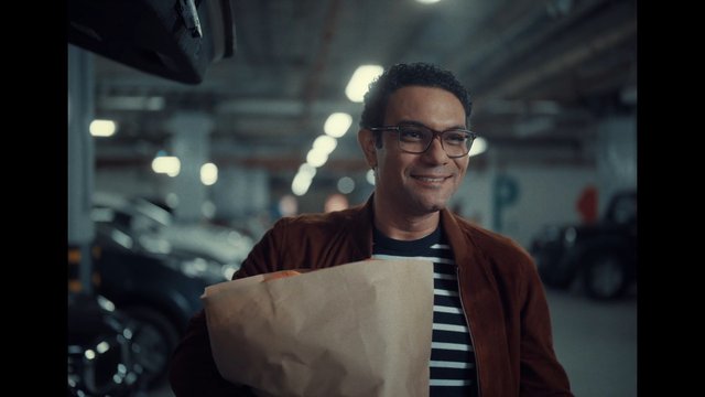 Video Reference: man, smiling, glasses, paper bag, grocery bag, parking garage, indoor parking, casual clothing, portrait, transportation, car, lifestyle, urban, shopping