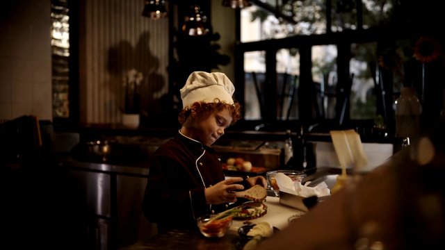 Video Reference: child, chef, cooking, kitchen, sandwich, food preparation, indoor, uniform, chef hat, counter, recipe, warm lighting, home kitchen, hands, meal prep