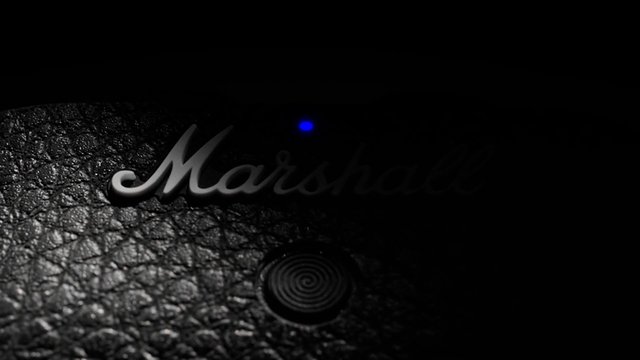 Video Reference: logo, text, close-up, dark, black surface, texture, metallic, indicator light, audio equipment, branding, product detail, low light
