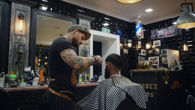 Video Reference: Shirt, Hat, Barware, Barber, Drinking establishment, Baseball cap, Chair, Beauty salon, T-shirt, Customer