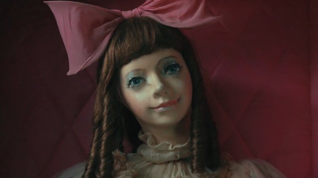 Video Reference: doll, girl, close-up, pink bow, red background, portrait, pale face, curly hair, frontal view, creepy, toy, fantasy