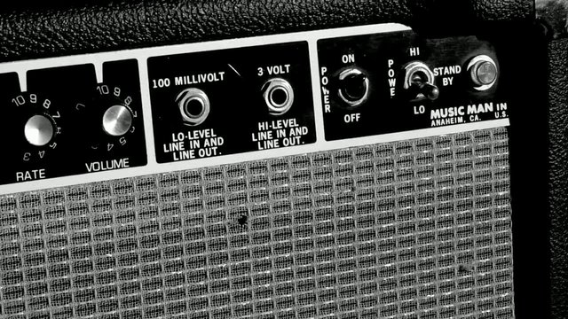 Video Reference: guitar amplifier, amp, control panel, knobs, input jacks, speaker grille, audio equipment, music gear, close-up, vintage, black and white, electronics