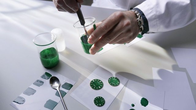 Video Reference: laboratory, hands, tweezers, beaker, chemical, sample, watch dial, green, testing, inspection, workbench, science, manufacturing, precision, close-up