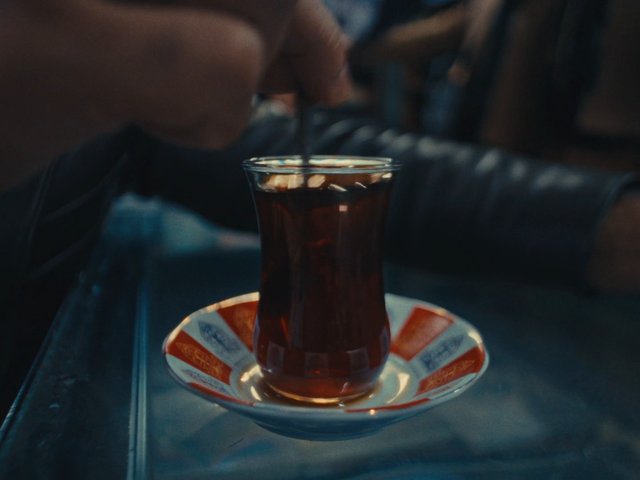 Video Reference: tea, glass, saucer, spoon, stirring, beverage, close-up, tableware, hot drink, refreshment, indoor, hand, drink