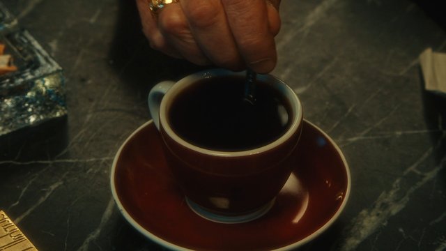 Video Reference: coffee, cup, saucer, stirring, hand, table, beverage, black coffee, close-up, indoor, drink, marble, cafe, still life
