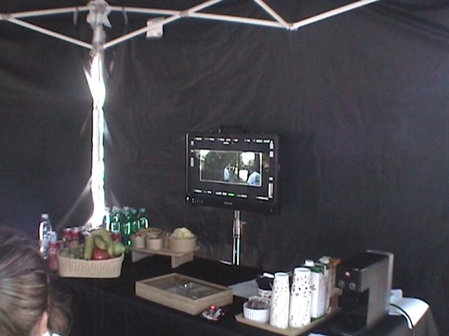 Video Reference: indoor, tent, booth, table, fruit, bottles, cups, monitor, video screen, equipment, dark, event, setup, display, snack table