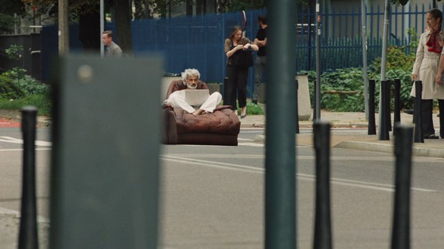 Video Reference: street, man, laptop, armchair, urban, pedestrians, outdoor, road, fence, greenery, sitting, barefoot, city, surreal