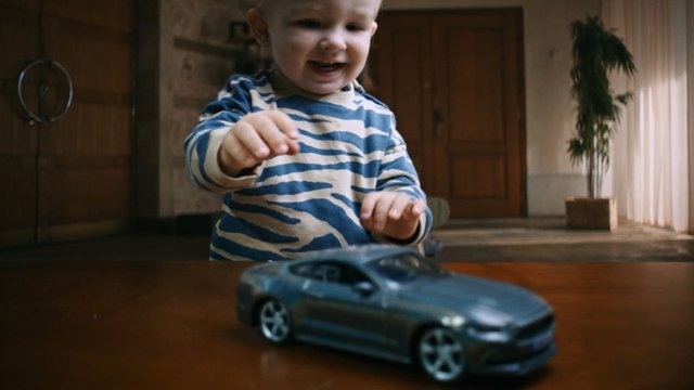 Video Reference: toddler, child, toy car, indoor, play, smiling, wooden table, home, family, close-up, room, motion blur, casual, cute