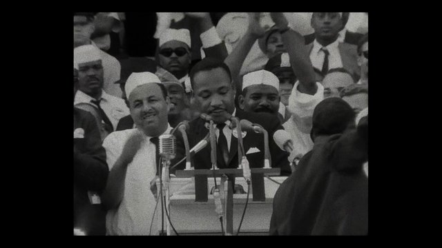 Video Reference: black and white, historical footage, speech, podium, microphones, crowd, political rally, public event, men, vintage, archival, speaker, gathering