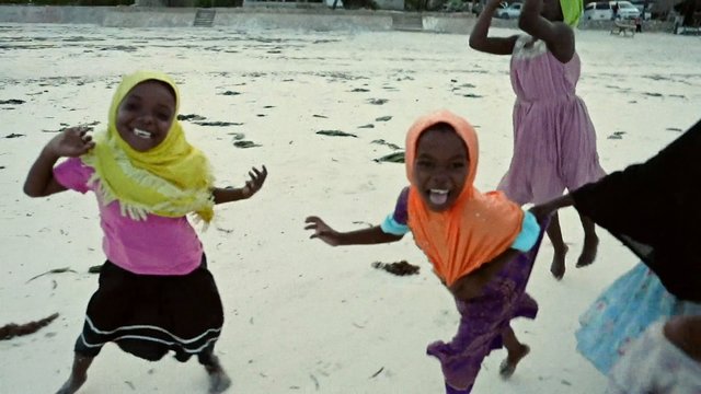 Video Reference: children, beach, sand, smiling, play, headscarf, colorful clothing, outdoor, group, joy, travel, vacation, coast, water, africa