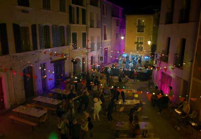Video Reference: night, street party, outdoor event, dancing, live music, band, string lights, courtyard, alley, festival, crowd, tables, stage, celebration, urban, warm lighting
