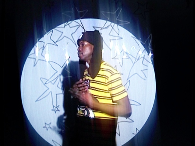 Video Reference: World, Flash photography, Sleeve, Gesture, Entertainment, Font, Performing arts, Window, T-shirt, Electric blue