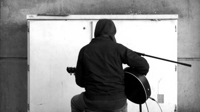 Video Reference: person, guitar, musician, back view, indoor, monochrome, performance, seated, instrument, wall, cabinet, practice, studio, solo