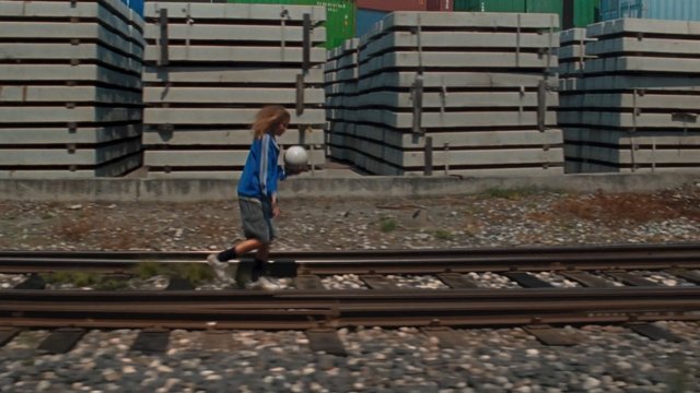 Video Reference: person, railroad tracks, walking, ball, blue jacket, outdoor, industrial, concrete barriers, motion, urban, transportation