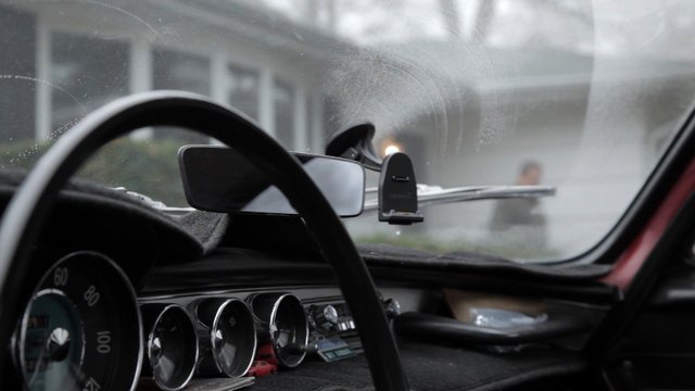 Video Reference: car interior, dashboard, steering wheel, windshield, phone mount, gauges, rainy, foggy, driving, vehicle, interior view, old car, blurred background, transportation