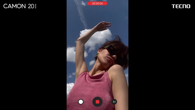 Video Reference: person, outdoors, sky, clouds, selfie, portrait, smartphone, video, pose, sunglasses, pink top, recording ui, advertisement, brand text