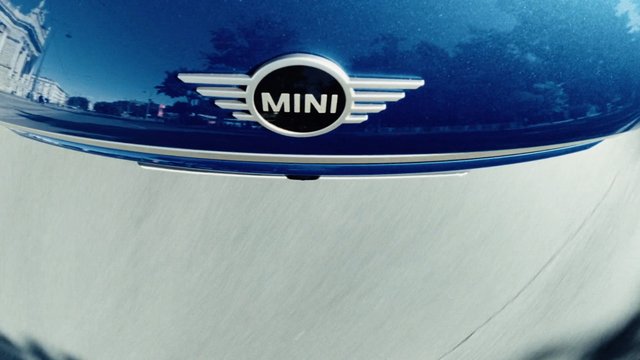 Video Reference: car, automobile, hood, emblem, logo, blue, white, close-up, front, vehicle, reflection, MINI, branding, transportation