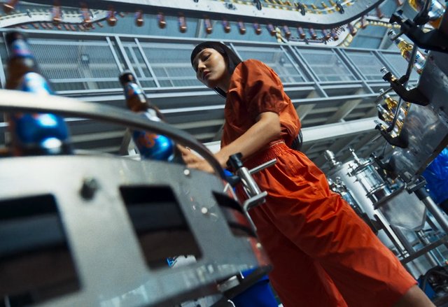 Video Reference: factory, industrial, worker, production, machinery, stainless steel, bottles, assembly line, low angle, orange outfit, manufacturing, equipment, automation, workplace, processing, operations