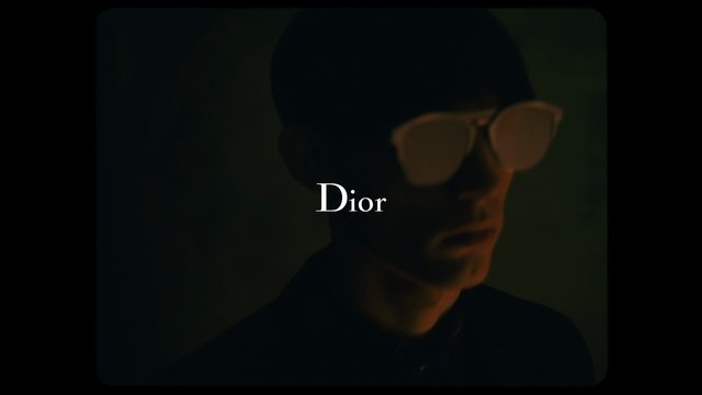 Video Reference: portrait, glasses, dark lighting, fashion, luxury, editorial, close-up, stylized, brand text, minimal, moody, advertisement
