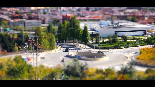 Video Reference: roundabout, city street, modern building, urban, aerial view, tilt-shift, intersection, trees, road, traffic, landscape, architecture, suburban, daytime