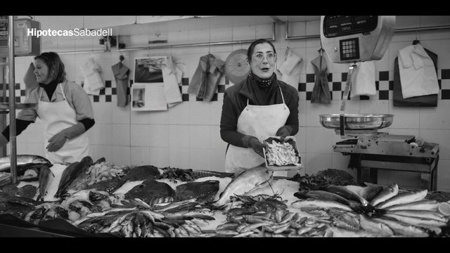 Video Reference: seafood, fish market, vendor, market stall, counter, ice display, apron, black and white, indoor, workplace, fresh fish, scale, food