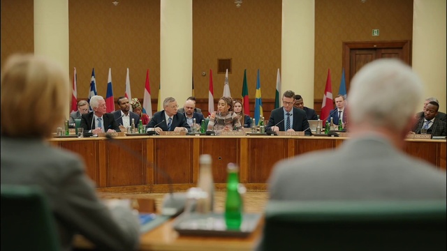 Video Reference: Microphone, Flag, Table, Suit, Water bottle, Official, Event, Public speaking, Speaker, Government