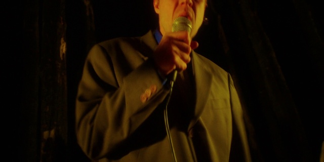 Video Reference: Dress shirt, Music, Entertainment, Facial hair, Event, Formal wear, Wood, Darkness, Audio equipment, Eyewear