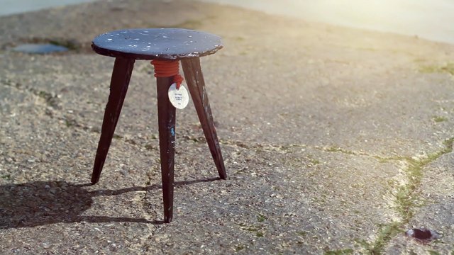 Video Reference: stool, wooden stool, three-legged, furniture, outdoor, sunlight, shallow depth of field, gravel, concrete, beach, shoreline, minimalism, still life, rustic