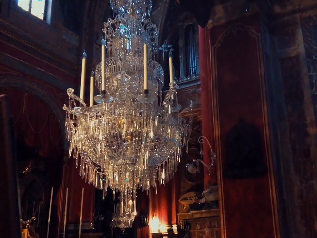 Video Reference: chandelier, crystal, interior, ornate, luxury, drapes, red curtains, dimly lit, historic, decorative, lighting, hall, elegant, classical, architecture, indoor