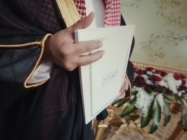 Video Reference: close-up, hands, certificate, document folder, formal attire, traditional clothing, ceremony, flowers, bouquet, indoor, event, celebration, decorative, patterned background