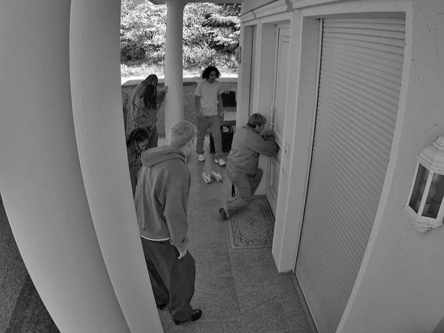 Video Reference: security camera, porch, house, people, outdoor, black and white, door, crouching, group, residential, covered patio, home exterior