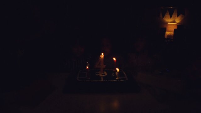 Video Reference: birthday, cake, candles, number 4, dark room, indoor, celebration, party, low light, dessert, table, warm light